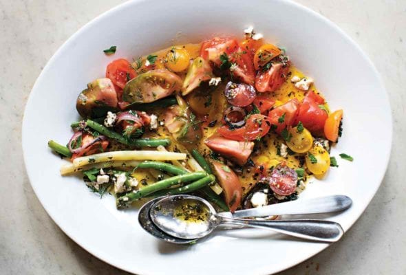 White plate of tomato and green bean salad with feta, red onion, parsley, and mint