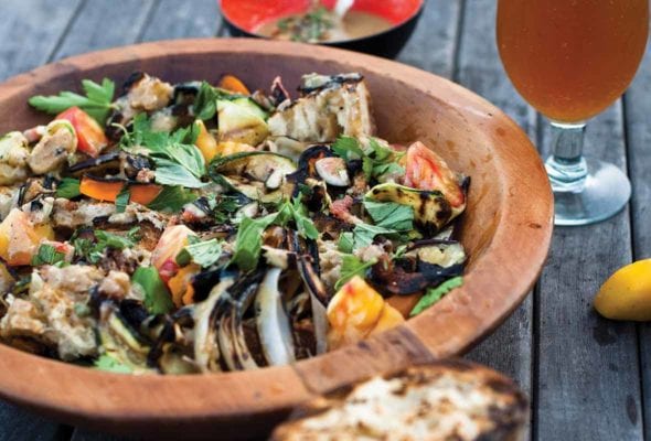 A wooden bowl filled with Catalan bread salad and a frothy beer on the side.