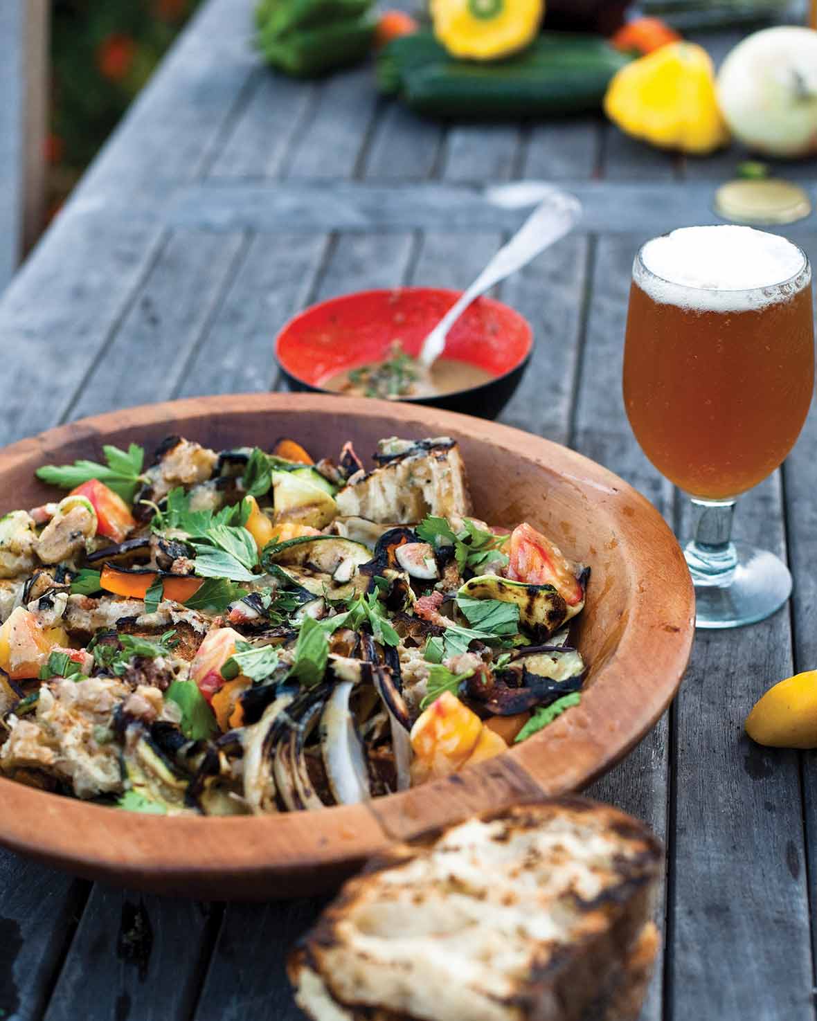 A wooden bowl filled with Catalan bread salad and a frothy beer on the side.