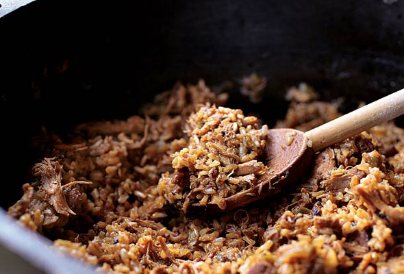 A cast-iron pot of chicken and sausage jambalaya with a wooden spoon resting inside.
