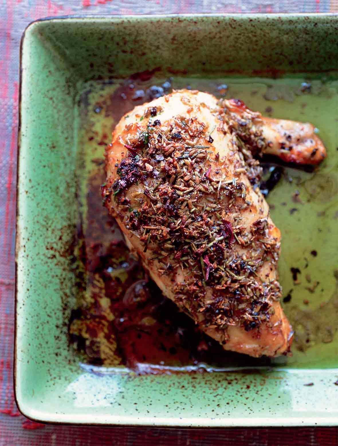 Lavender and honey glazed chicken leg and thigh topped with lavender flowers on a green plate