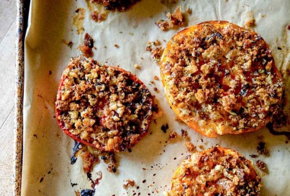 Several halves of tomato Provençal on a parchment-lined rimmed baking sheet.