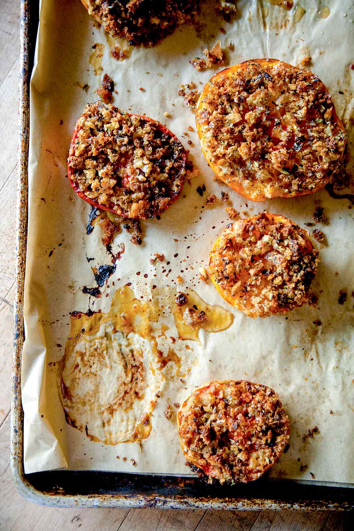 Several halves of tomato Provençal on a parchment-lined rimmed baking sheet.