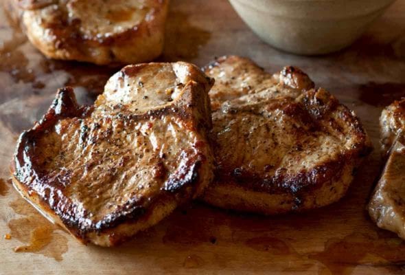 Four juicy seared maple-brined pork chops with pear chutney on a cutting board