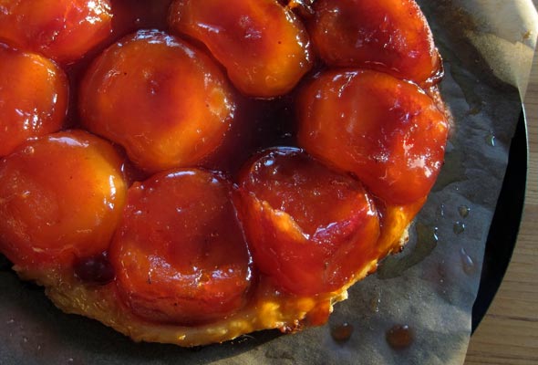 A tarte tatin on a piece of parchment paper resting on a black plate.