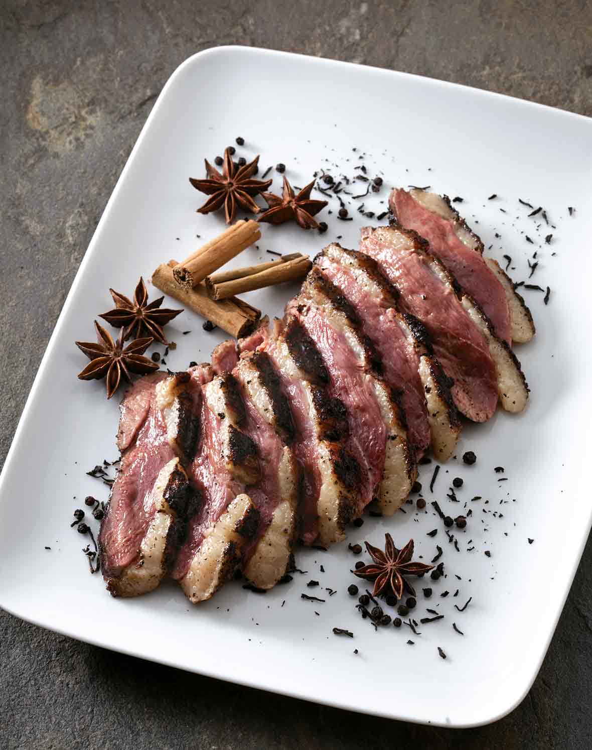 Sliced tea-smoked duck breast on a square white plate with star anise and loose tea