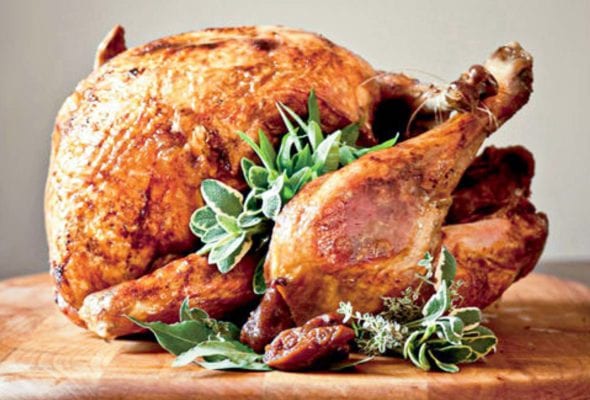 A whole deep-fried turkey, garnished with sage, bay, and thyme leaves on a wooden cutting board.