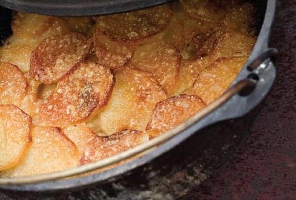 A partially covered Dutch oven filled with cooked Parmesan potato gratin.