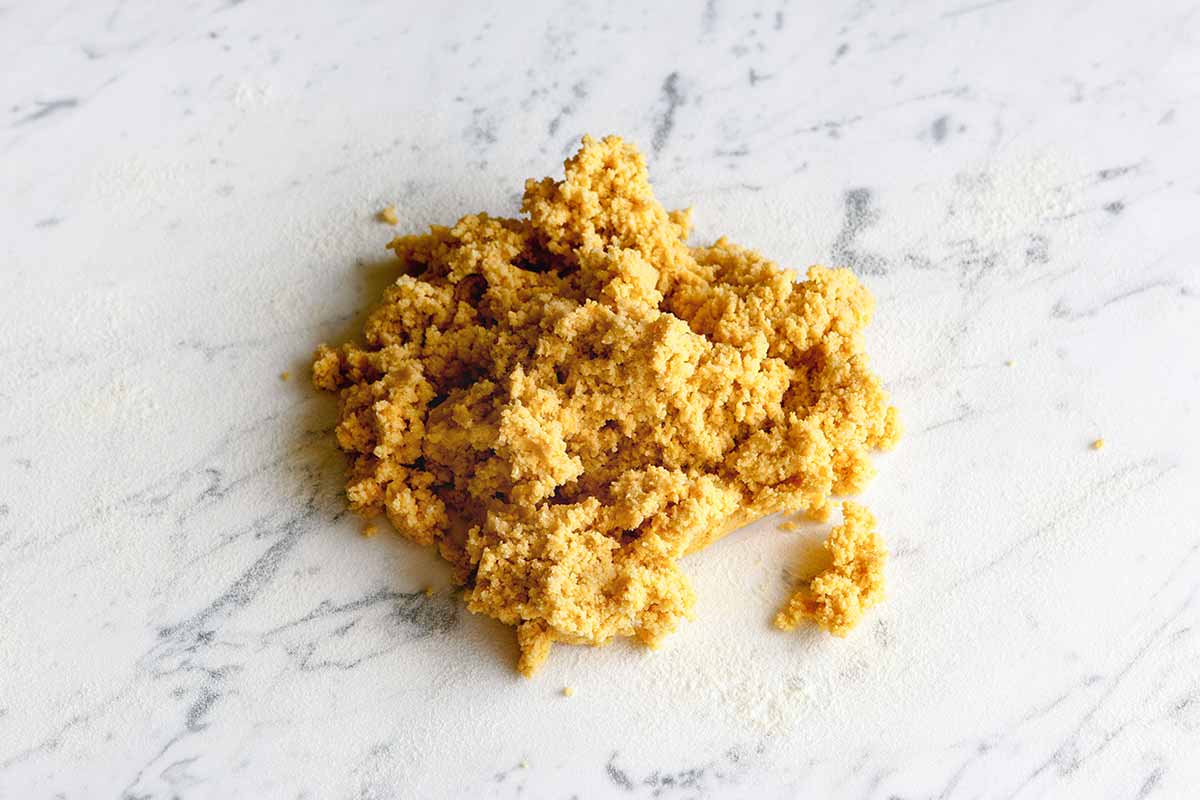 A pile of pumpkin pasta dough on a white and grey marble surface.