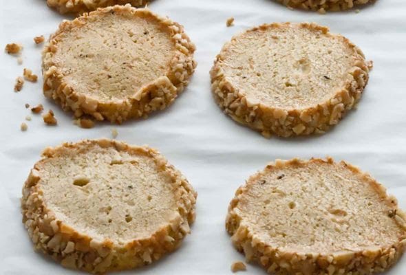 Four delicate Stilton Walnut crackers, edges rolled in chopped walnuts, on a parchment-lined sheet pan