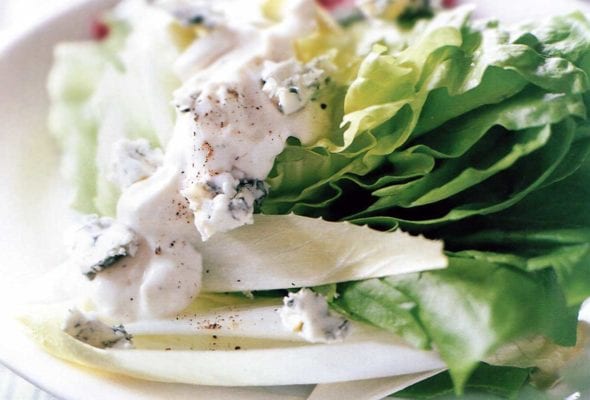 A Bibb wedge, radicchio, endive, and blue cheese dressing on a white plate set on top of blue and yellow linens.