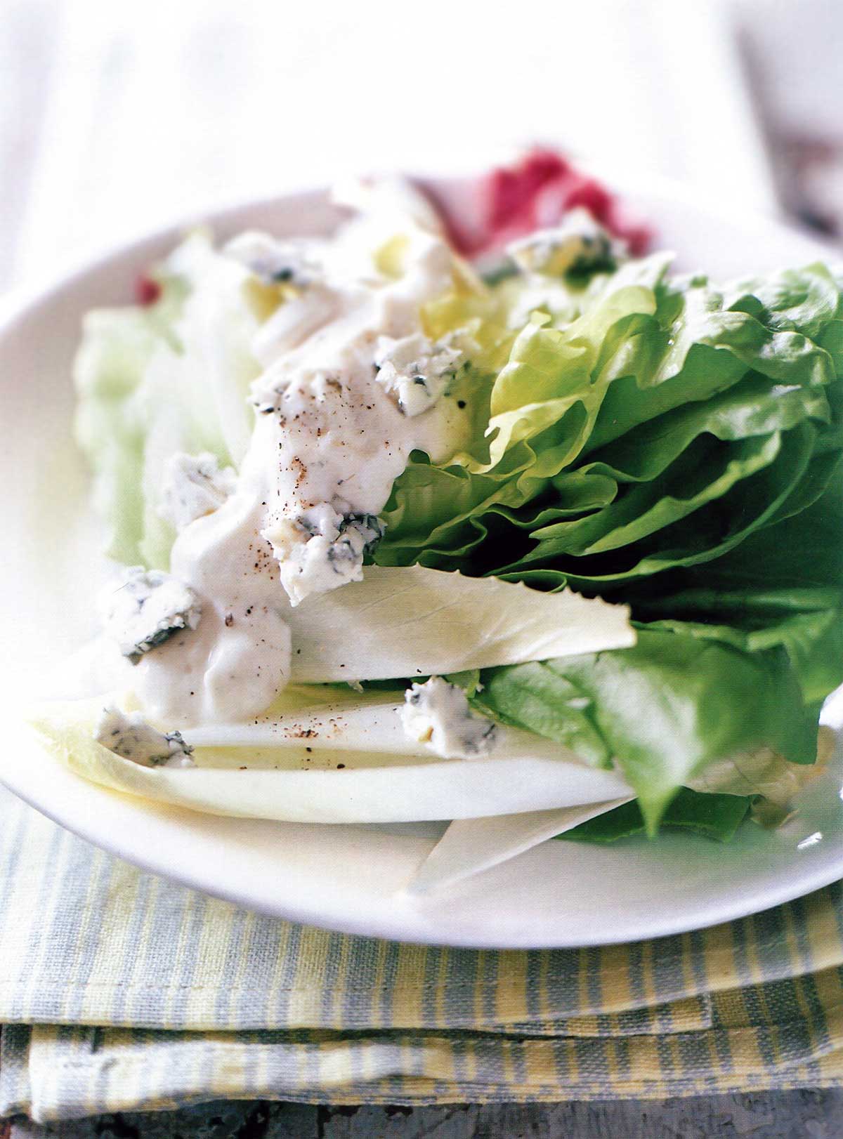 A Bibb wedge, radicchio, endive, and blue cheese dressing on a white plate set on top of blue and yellow linens.