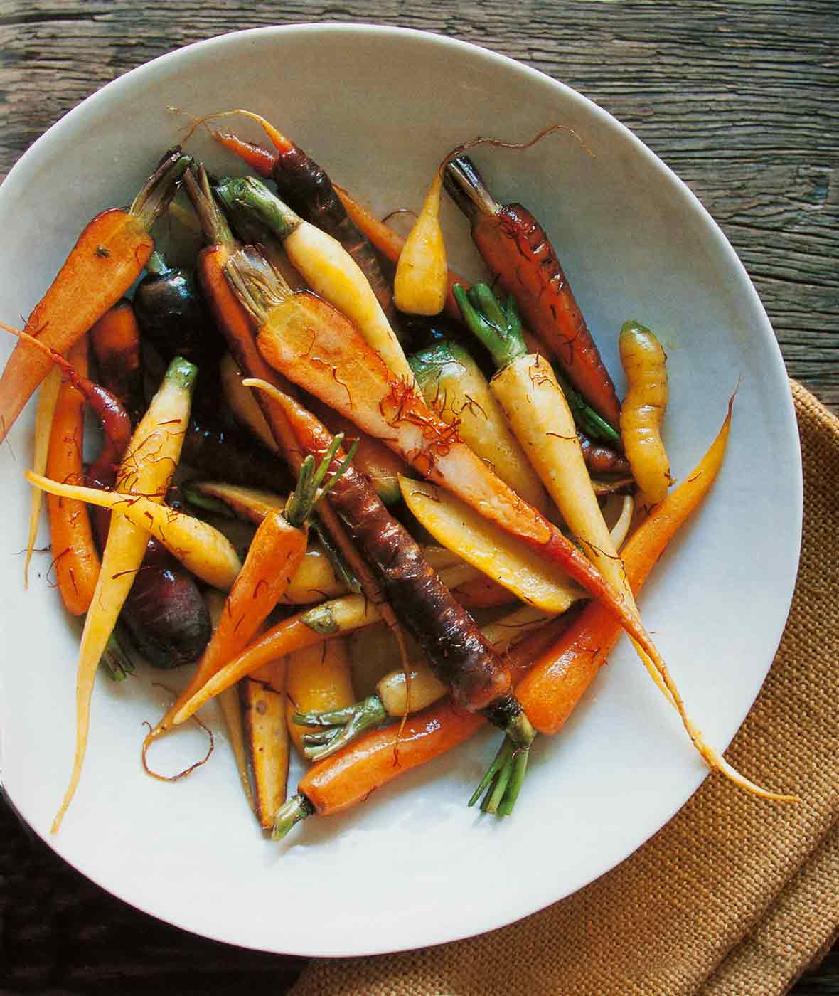 A white bowl of braised saffron carrots on a piece of burlap on a wooden table.