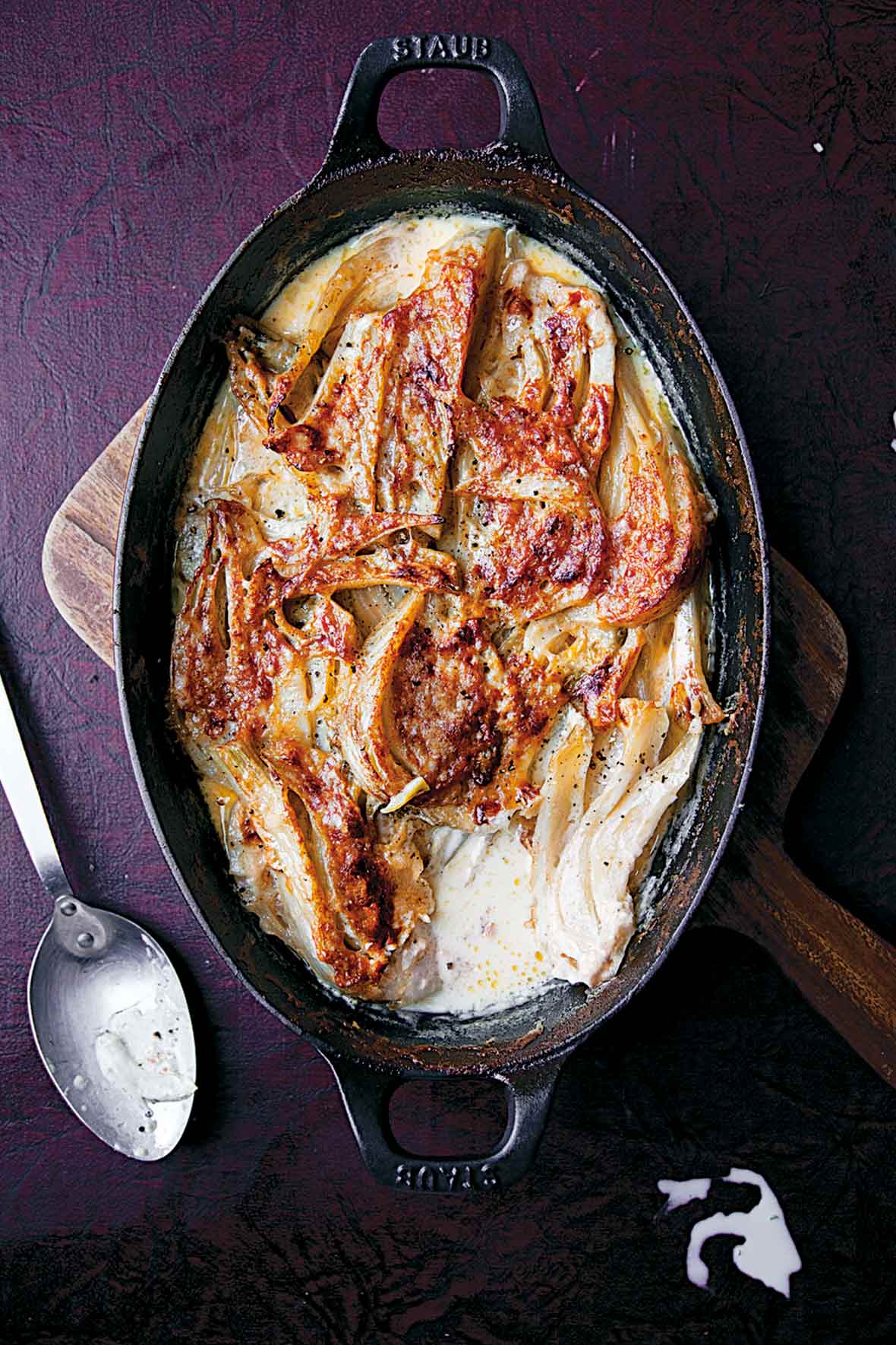 A cast-iron baking dish filled with fennel baked in cream on a wooden board.