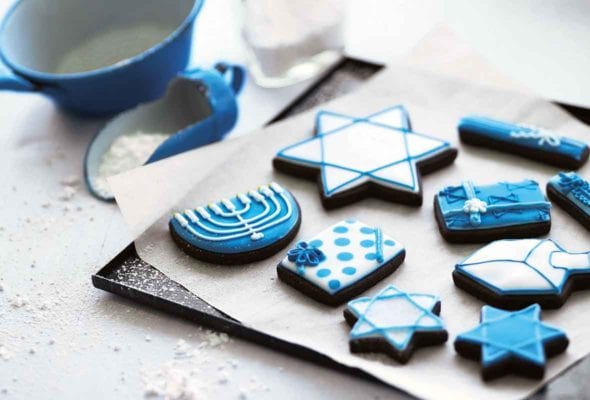 A selection of frosted cookies decorated for Hanukkah, on a parchment-lined cookie sheet