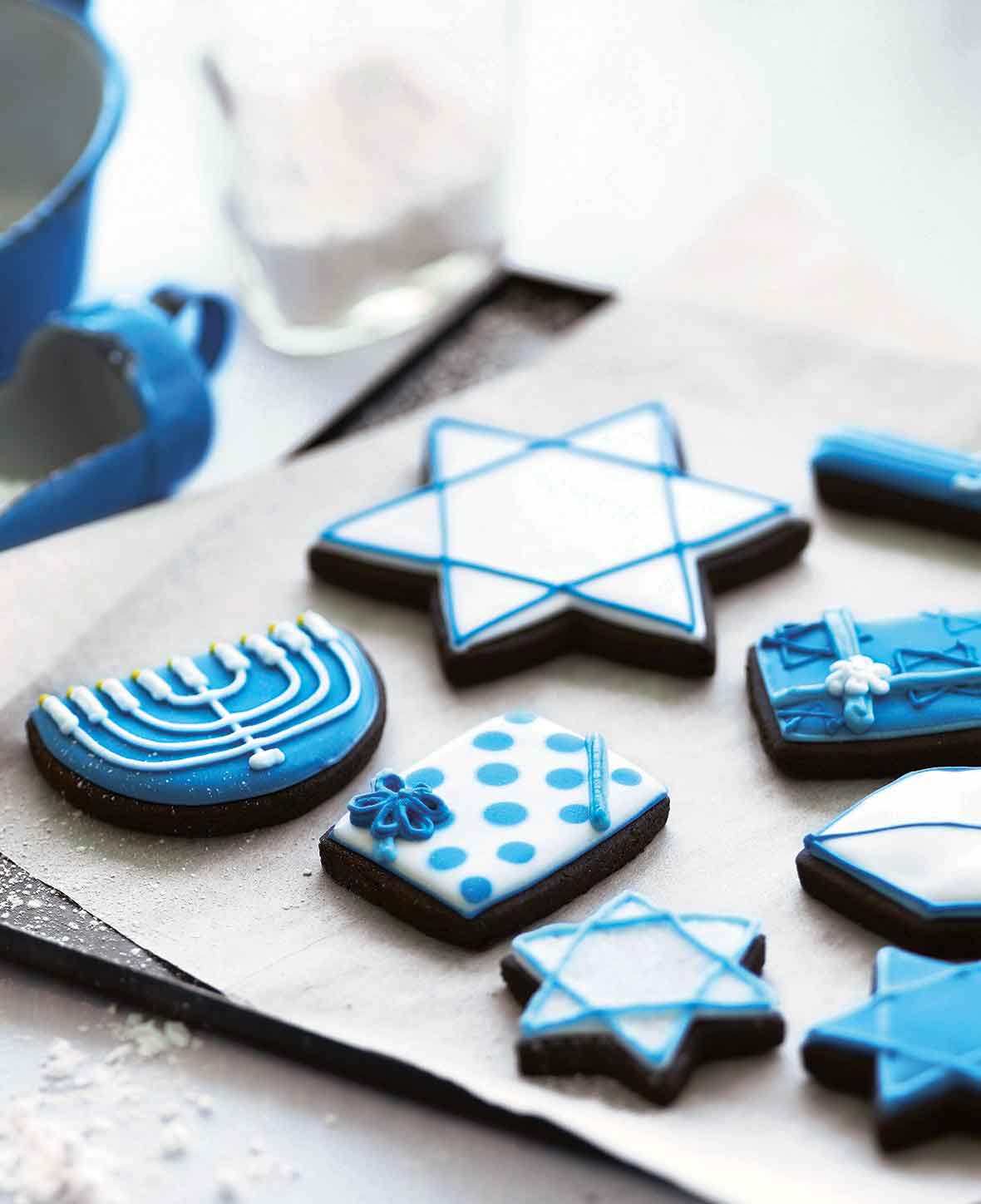 A selection of frosted cookies decorated for Hanukkah, on a parchment-lined cookie sheet