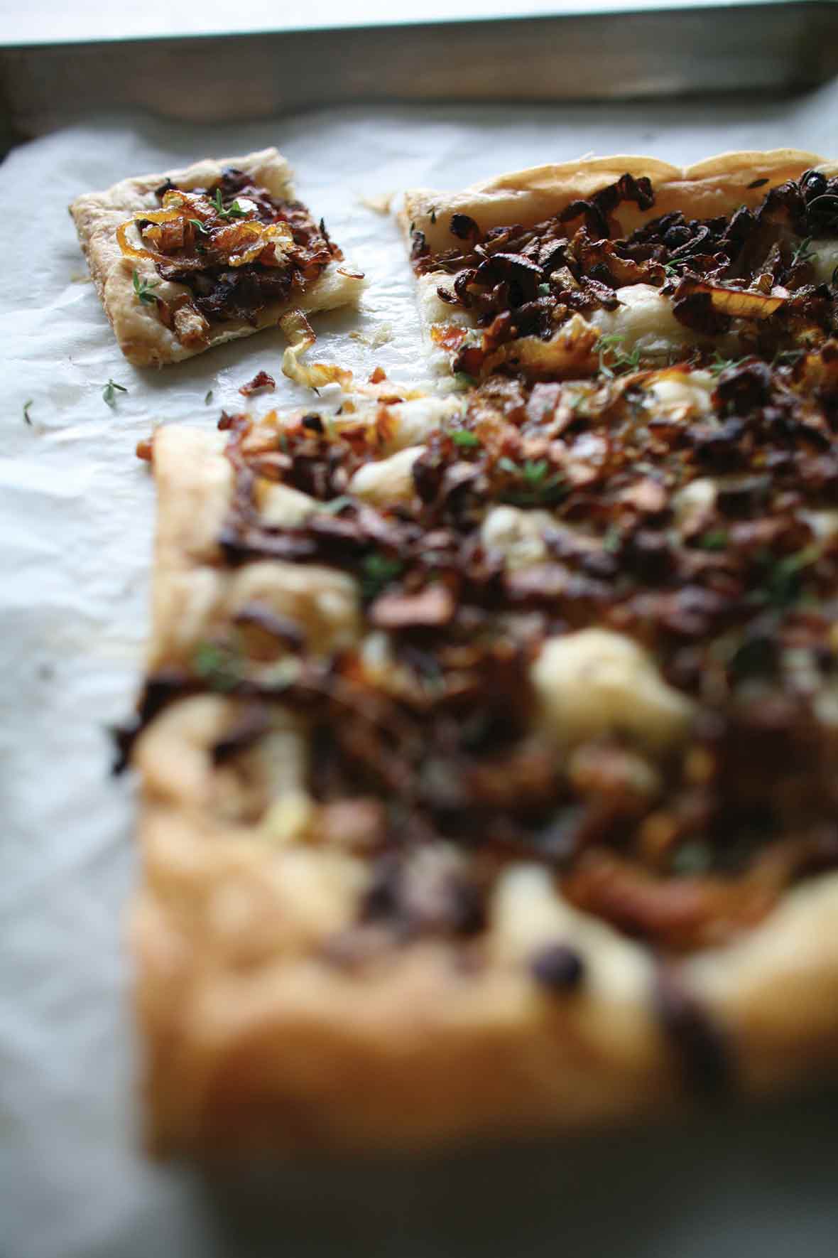 A sheet pan with n onion thyme tart on it, covered with cooked onions, thyme on a puff pastry crust