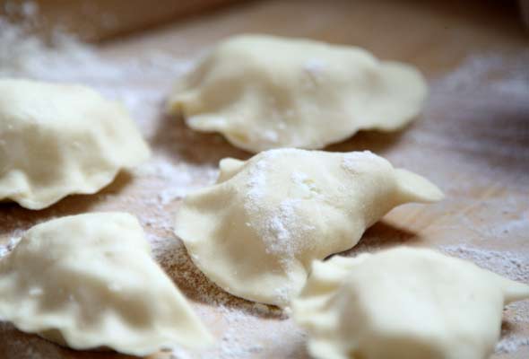Five uncooked floured pierogi on a wooden board.