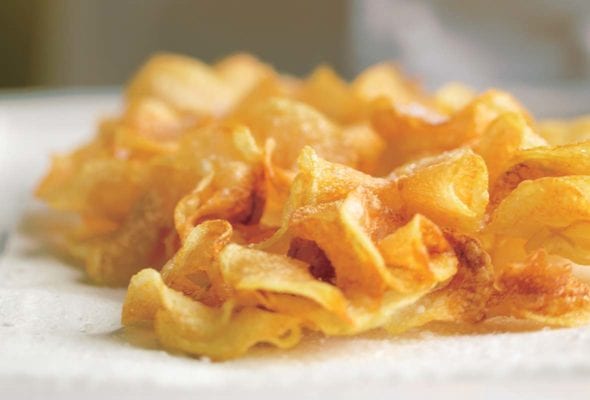 A pile of homemade potato ruffles on a white surface.