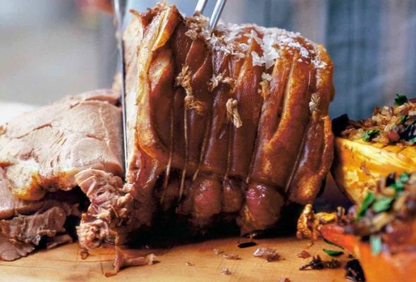 Slow-roasted pork shoulder of a cutting board being sliced by a person