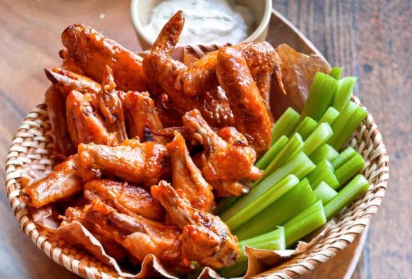 A basket of broiled buffalo wings with celery sticks and blue cheese dressing.