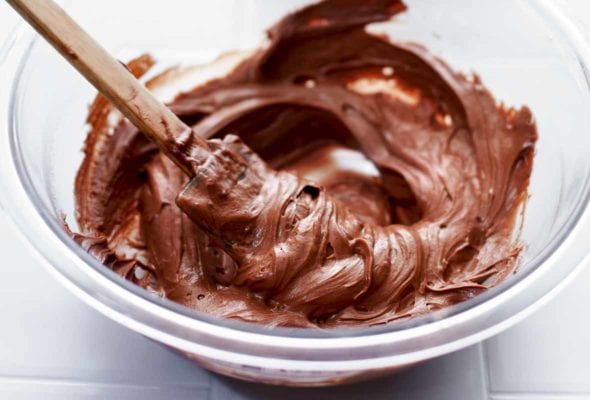 A glass mixing bowl filled with homemade nutella and a spatula rests inside the bowl