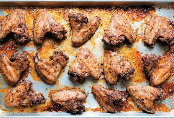 A rimmed baking sheet filled with peppery chicken wings