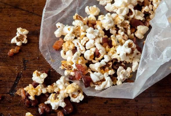 Open waxed paper bag with popcorn and maple bacon bits spilling out