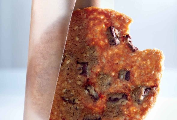 One ultra-thin chocolate chunk cookie resting against a roll of wax paper.