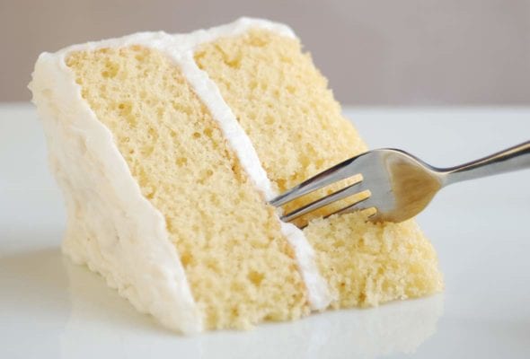 A wedge of classic white cake and white frosting with a fork cutting in