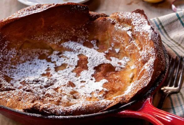 Cast-iron skillet with a Dutch baby--a popover pancake--topped with powder sugar on a set breakfast table