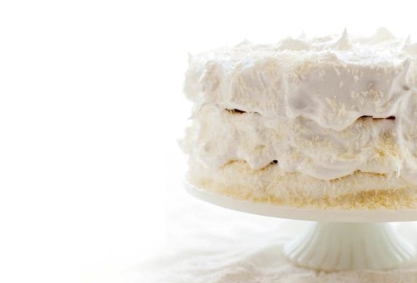 A 3-layer coconut angel food cake covered in white frosting on a white cake stand