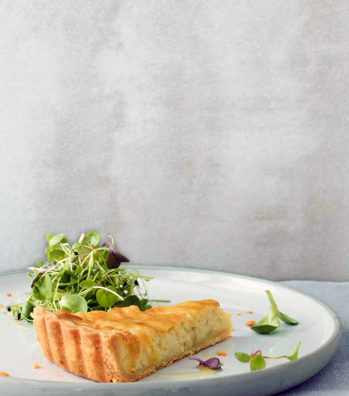 A slice of a creamy onion tart, with a flaky crust and tossed mixed salad on a white plate