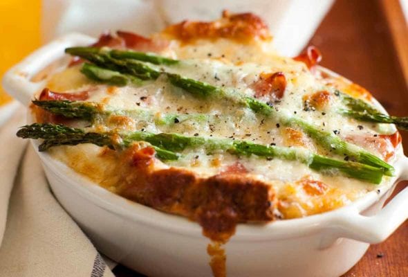 A white oval casserole filled with asparagus, egg and cheese strata--bread, Fontina cheese, eggs, prosciutto, and asparagus