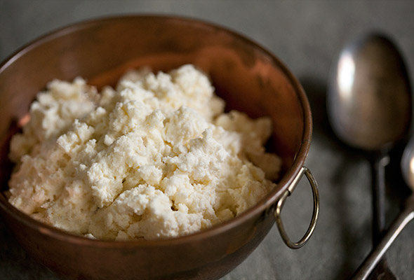 A bowl filled with fresh whole milk ricotta and a spoon on the side.
