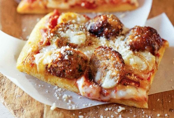 Three square slices of meatball pizza on strips of parchment paper, with fresh Parmesan sprinkled overtop.