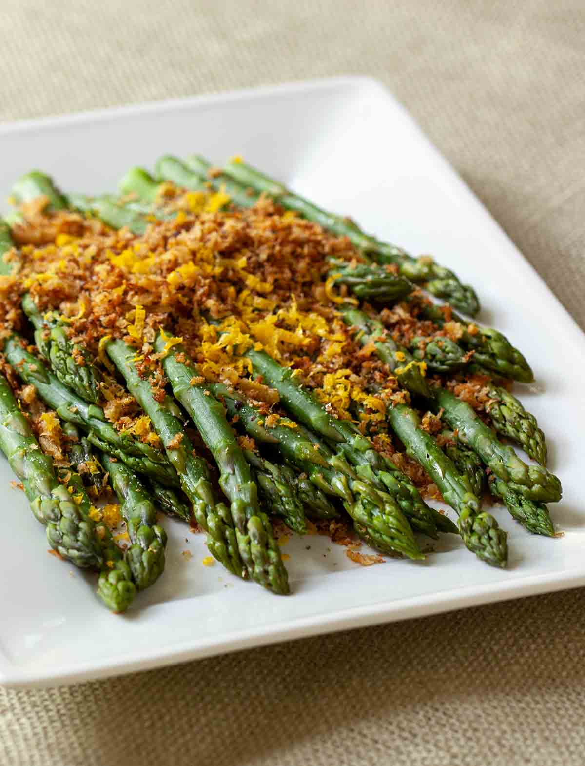Asparagus with brioche crumbs piled on a white serving platter.
