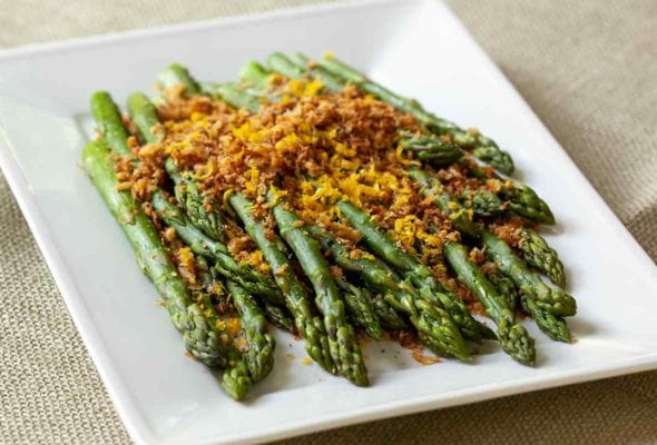 Asparagus with brioche crumbs piled on a white serving platter.