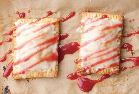 Two homemade toaster tarts on a sheet of parchment drizzled with glaze.