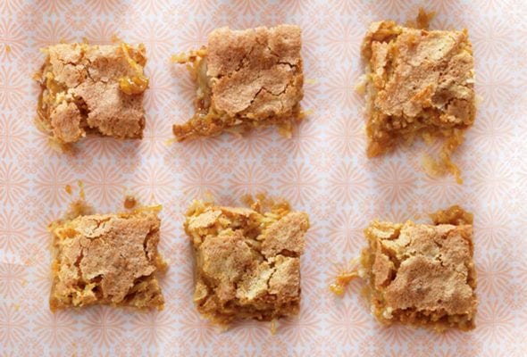 A white baking dish with a piece of patterned parchment and 15 squares of coconut blondies.