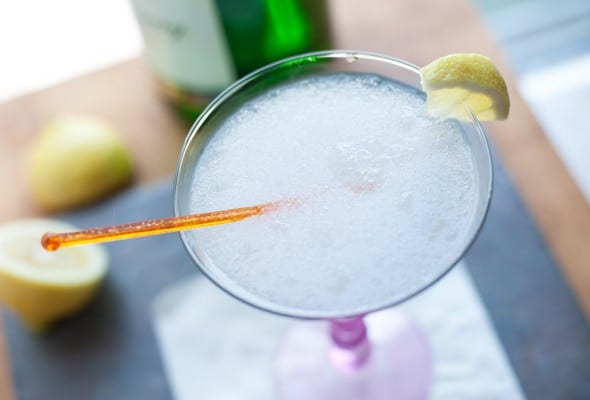A frozen gin fizz in a martini glass with an orange stir stick and a little piece of lemon on the rim.