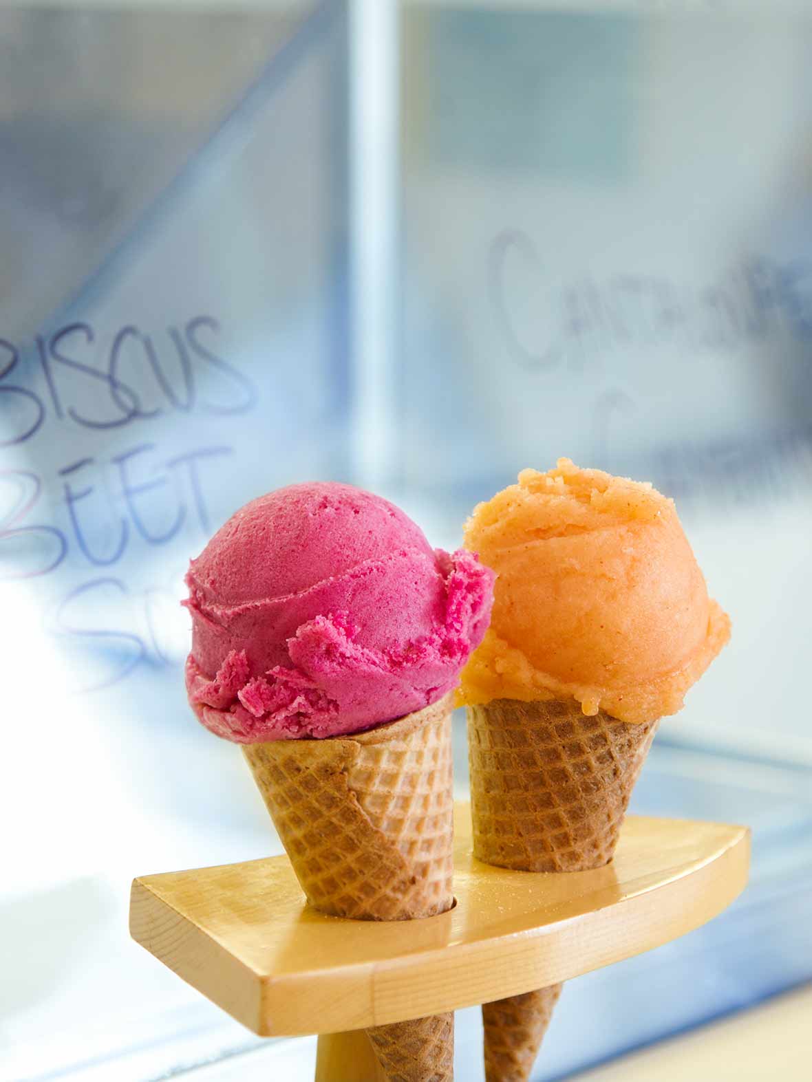 Two sugar cones, one filled with a scoop of cantaloupe sorbet, the other with a scoop of hibiscus beet sorbet.