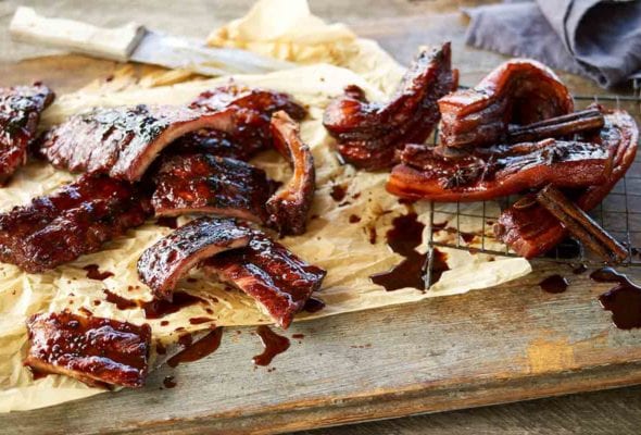 Sticky pork ribs cut into individual ribs on a piece of parchment with a knife.