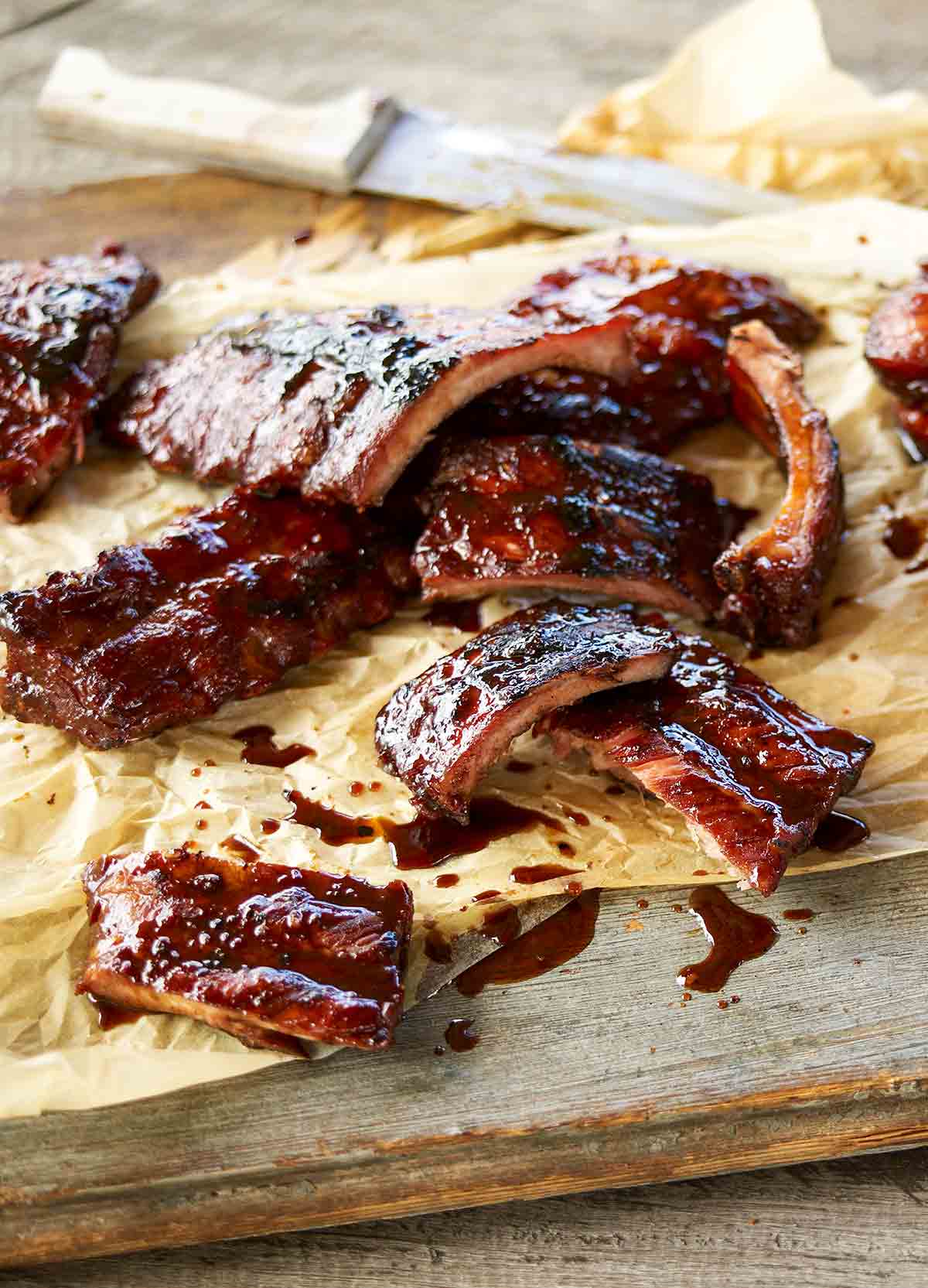 Sticky pork ribs cut into individual ribs on a piece of parchment with a knife.