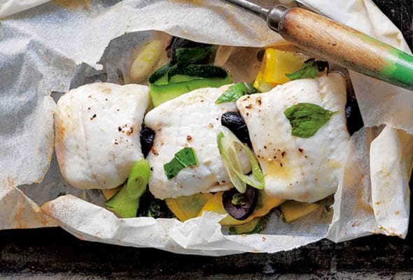 A rimmed baking sheet with fish in parchment and a fish spatula resting beside it.
