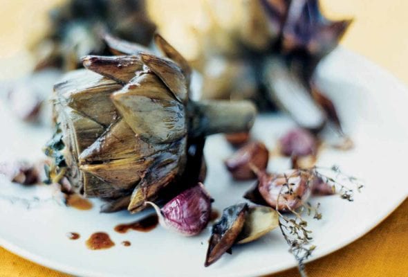 Three braised artichokes with garlic and thyme on a white plate.