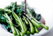 A white plate of broccoli rabe with balsamic brown butter being poured on top
