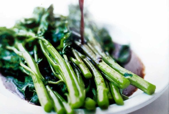 A white plate of broccoli rabe with balsamic brown butter being poured on top