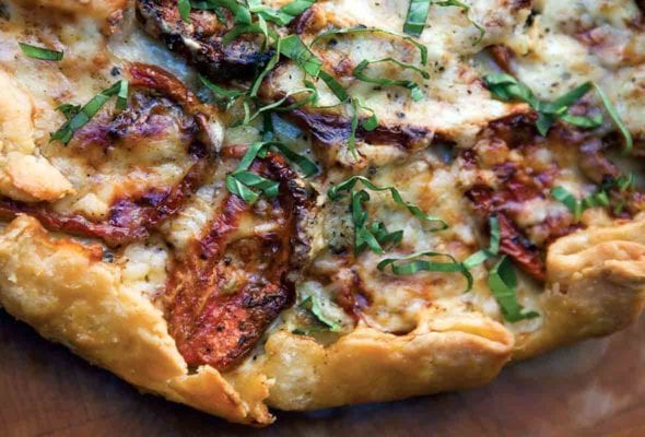 A close up view of a roasted tomato-basil tart encased in flaky pastry and smothered in cheddar.