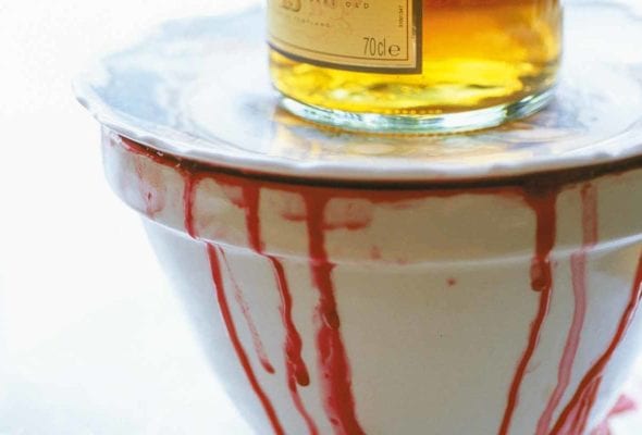 A white bowl with wine dripping down the side topped with a white plate and a bottle of whiskey.